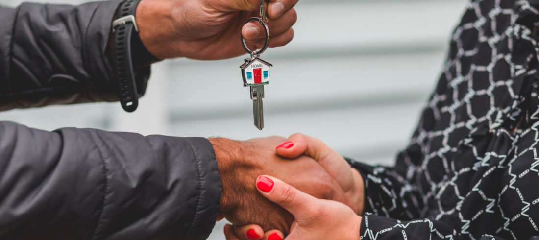 A real estate agent shakes hands with a client who holds a key after a successful closing.