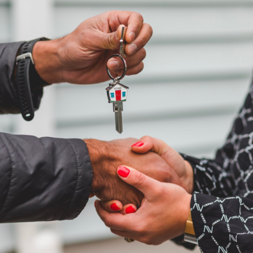 A real estate agent shakes hands with a client who holds a key after a successful closing.