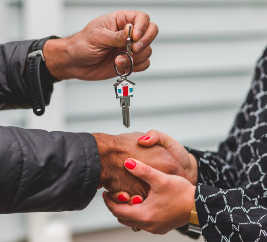 A real estate agent shakes hands with a client who holds a key after a successful closing.