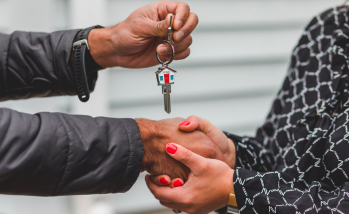 A real estate agent shakes hands with a client who holds a key after a successful closing.