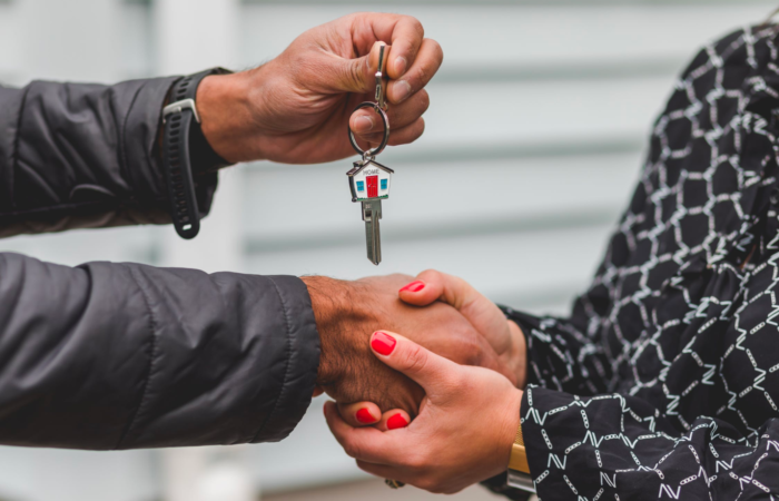 A real estate agent shakes hands with a client who holds a key after a successful closing.