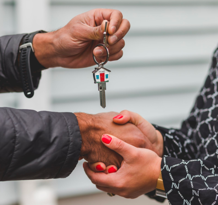 A real estate agent shakes hands with a client who holds a key after a successful closing.