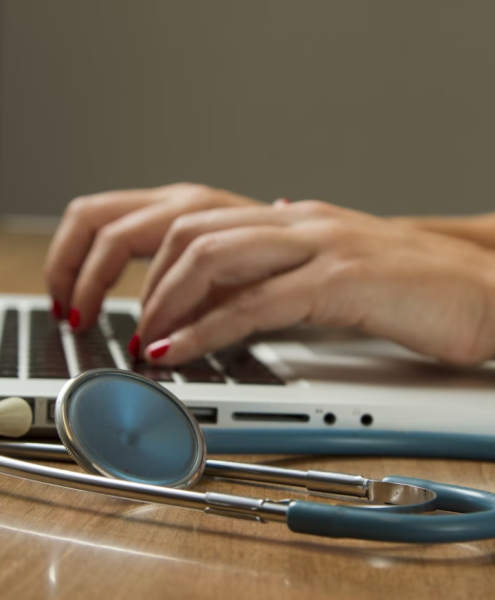 A healthcare administrator works on their laptop with a stethoscope beside them.