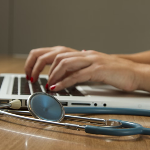 A healthcare administrator works on their laptop with a stethoscope beside them.