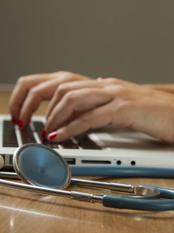 A healthcare administrator works on their laptop with a stethoscope beside them.