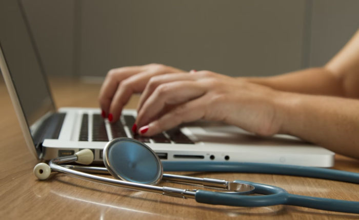 A healthcare administrator works on their laptop with a stethoscope beside them.