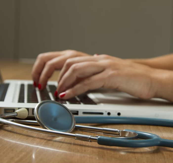 A healthcare administrator works on their laptop with a stethoscope beside them.