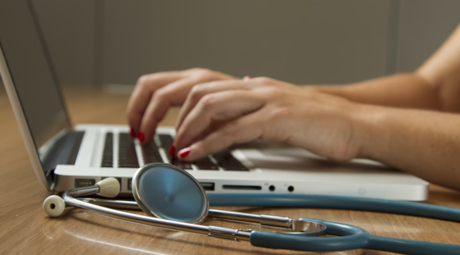 A healthcare administrator works on their laptop with a stethoscope beside them.