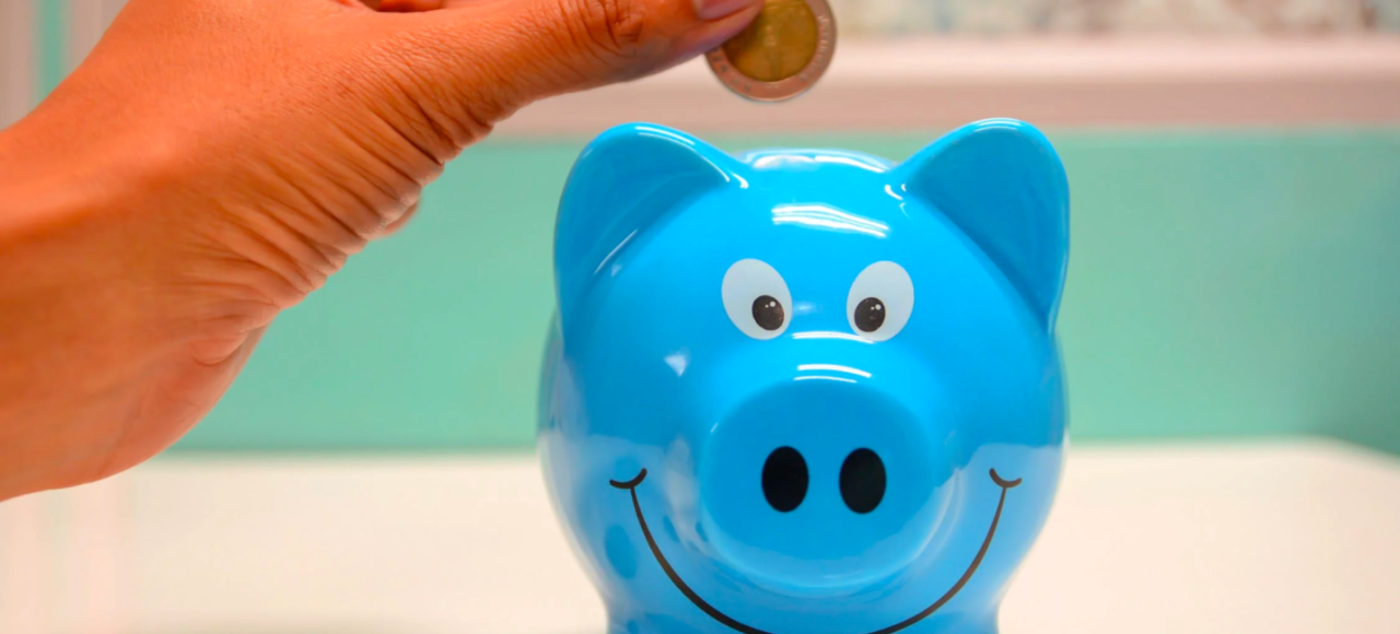 A person inserts coins into a piggy bank to save