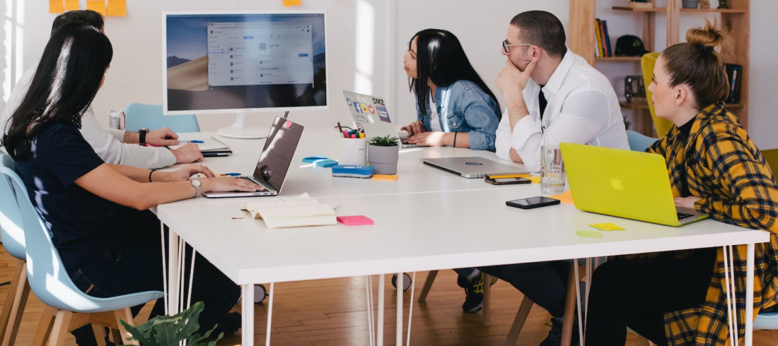 Employees in an office work around a table during a presentation.