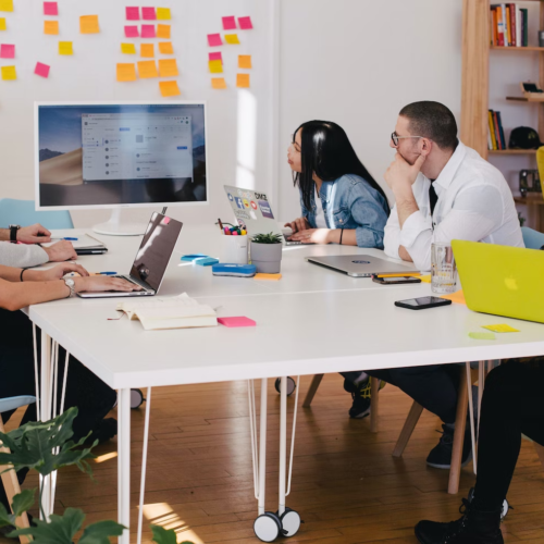 Employees in an office work around a table during a presentation.