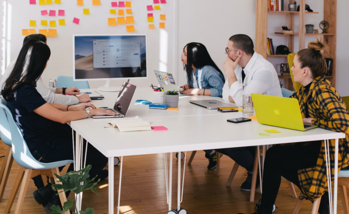 Employees in an office work around a table during a presentation.