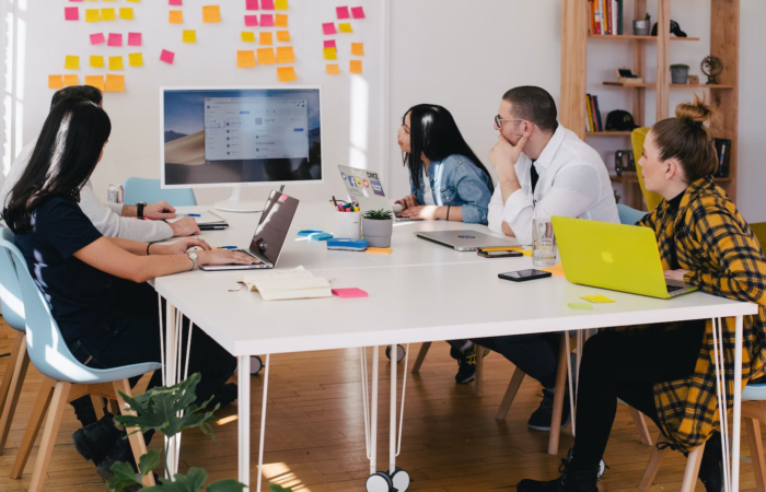 Employees in an office work around a table during a presentation.