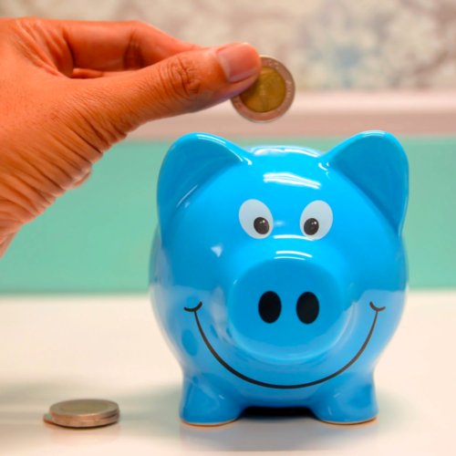 A person inserts coins into a piggy bank to save