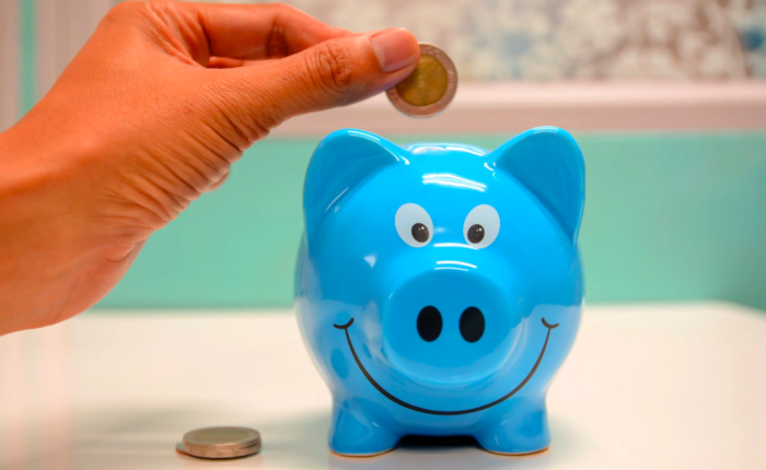 A person inserts coins into a piggy bank to save