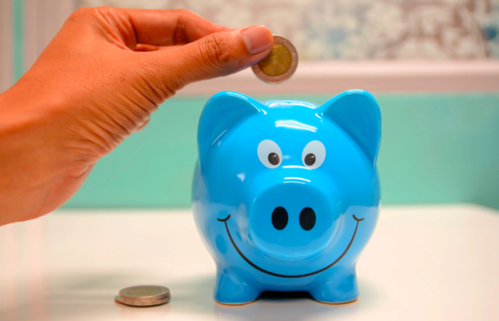 A person inserts coins into a piggy bank to save