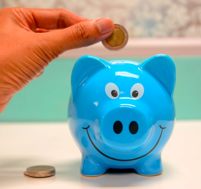 A person inserts coins into a piggy bank to save