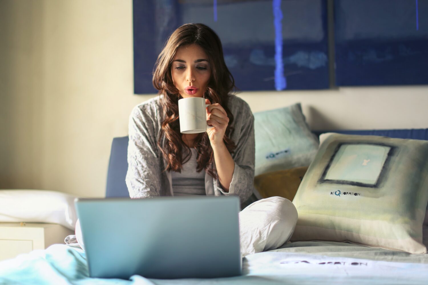 a young employee sitting on the bed with her coffee and work laptop