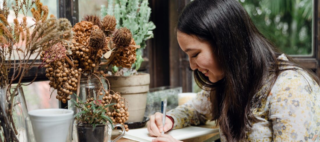 a woman writing in front of a floral arrangement