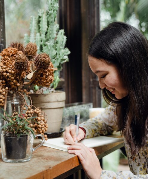 a woman writing in front of a floral arrangement