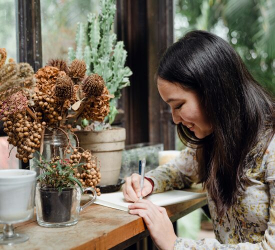 a woman writing in front of a floral arrangement