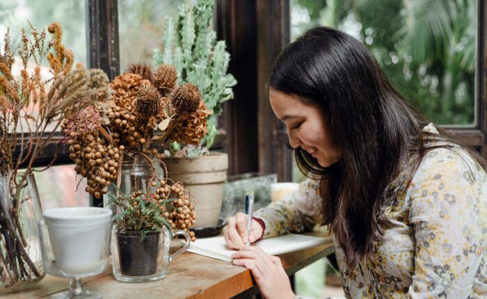 a woman writing in front of a floral arrangement