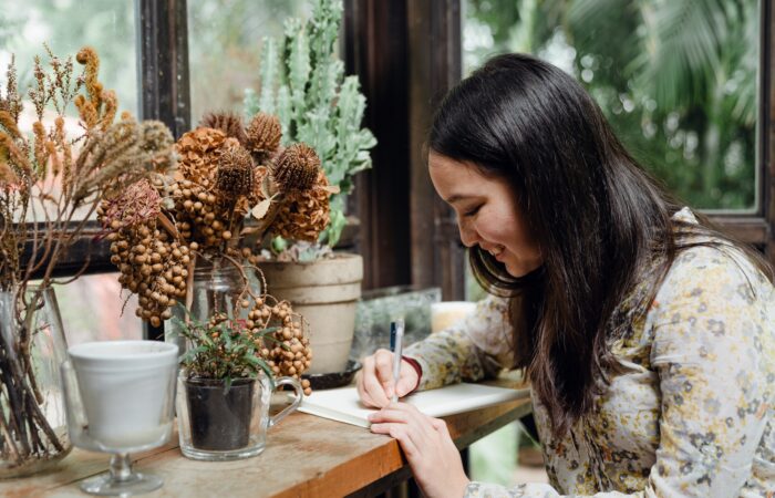 a woman writing in front of a floral arrangement