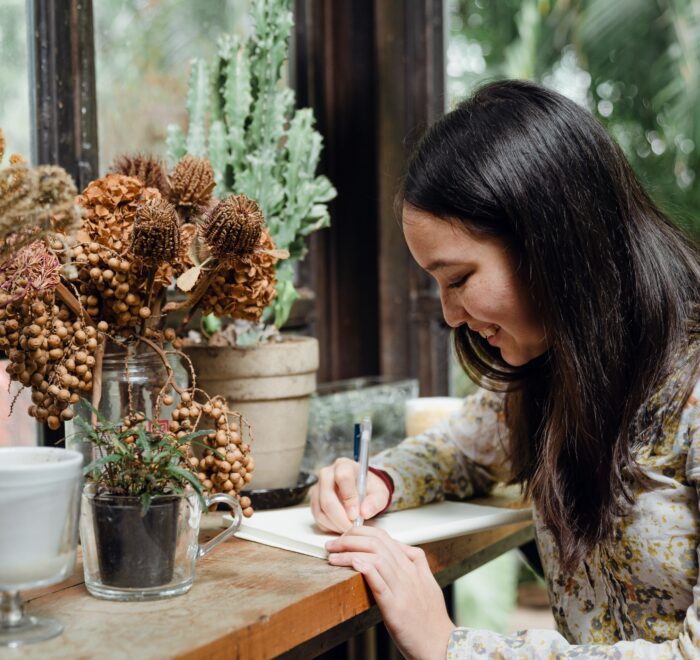 a woman writing in front of a floral arrangement