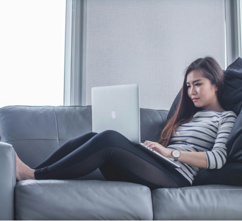 a woman lying on the couch and working on her computer