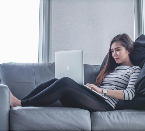 a woman lying on the couch and working on her computer