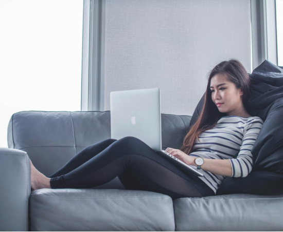 a woman lying on the couch and working on her computer