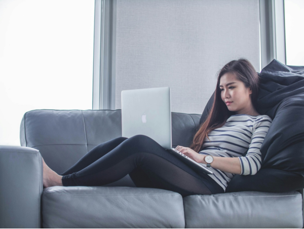 a woman lying on the couch and working on her computer