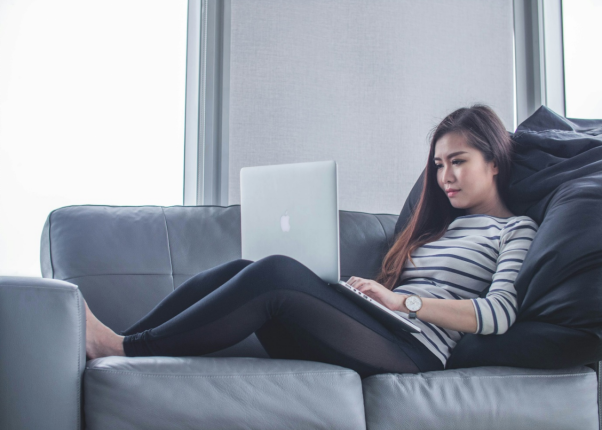 a woman lying on the couch and working on her computer