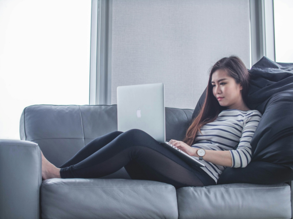 a woman lying on the couch and working on her computer